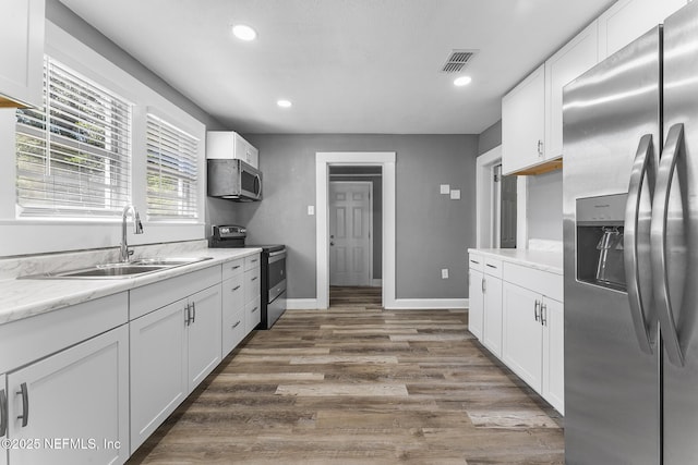 kitchen featuring dark wood-type flooring, sink, white cabinetry, light stone counters, and appliances with stainless steel finishes