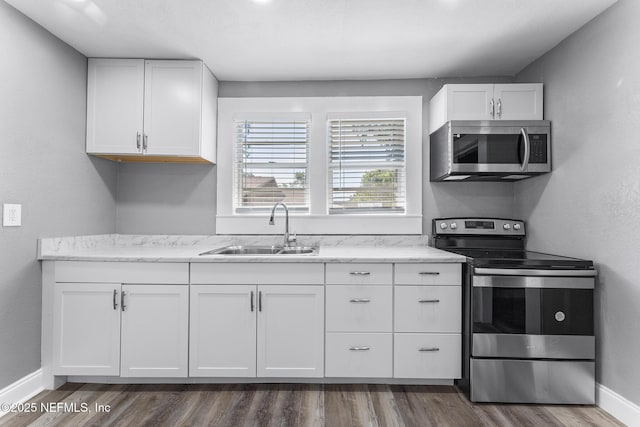 kitchen with appliances with stainless steel finishes, sink, white cabinets, light stone countertops, and dark wood-type flooring