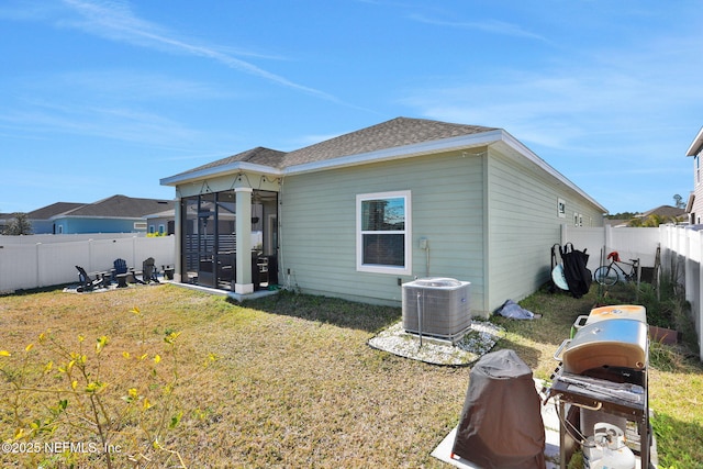 back of property with central AC, a sunroom, and a lawn