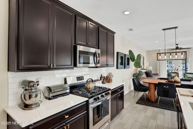 kitchen featuring hanging light fixtures, dark brown cabinets, stainless steel appliances, tasteful backsplash, and light wood-type flooring