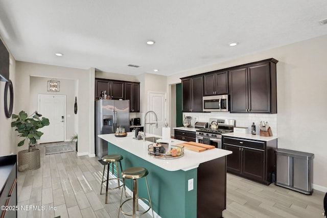 kitchen featuring sink, a breakfast bar area, appliances with stainless steel finishes, dark brown cabinetry, and an island with sink