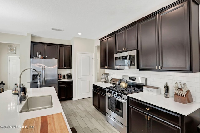 kitchen with sink, dark brown cabinets, stainless steel appliances, light hardwood / wood-style floors, and backsplash