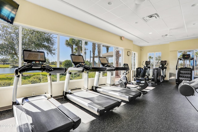 workout area with a water view, a healthy amount of sunlight, and a paneled ceiling