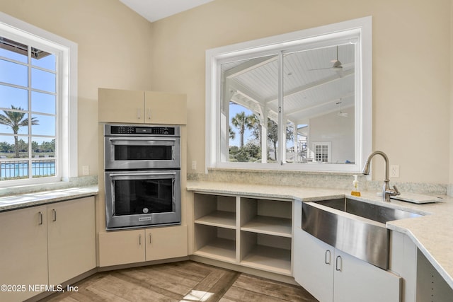 kitchen featuring double oven, sink, a water view, cream cabinets, and light wood-type flooring