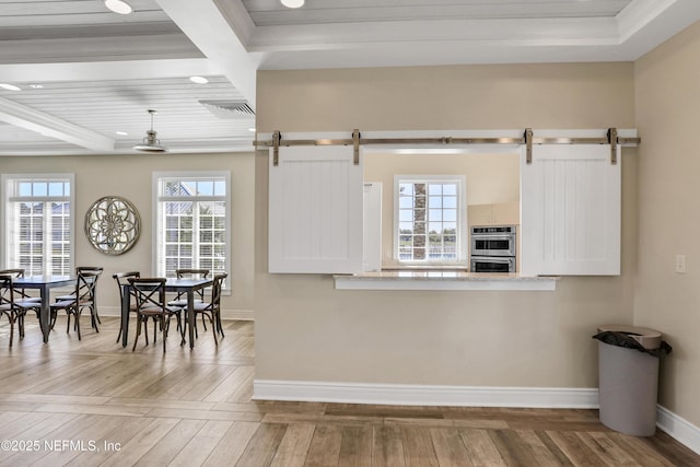 kitchen with ornamental molding, a barn door, stainless steel double oven, and white cabinets