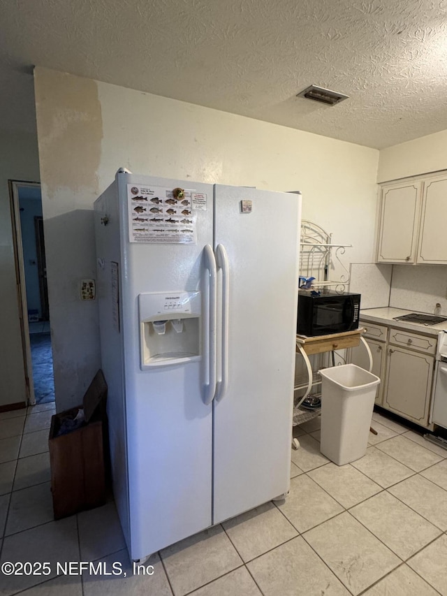 kitchen with white refrigerator with ice dispenser, light tile patterned floors, a textured ceiling, and white cabinets