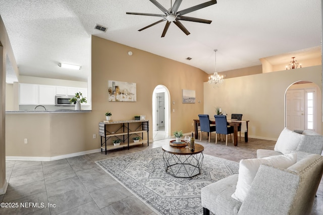 tiled living room with lofted ceiling, ceiling fan with notable chandelier, and a textured ceiling