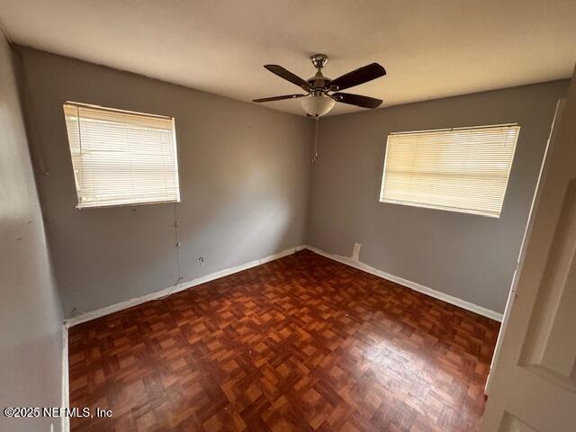 unfurnished room with ceiling fan and dark parquet flooring