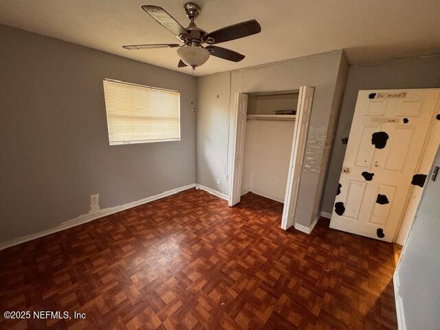 unfurnished bedroom featuring dark parquet flooring, ceiling fan, and a closet