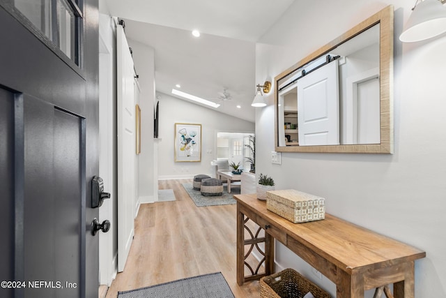 corridor with lofted ceiling with skylight, a barn door, and light hardwood / wood-style floors