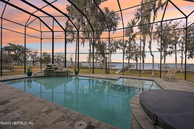 pool at dusk with a patio, a water view, and glass enclosure