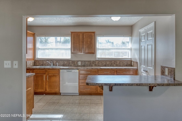 kitchen featuring white dishwasher, light tile patterned floors, a breakfast bar area, and a wealth of natural light