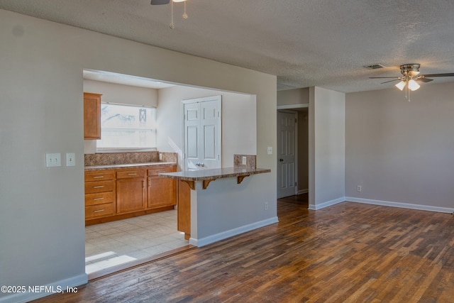 kitchen featuring light wood-type flooring, a breakfast bar area, ceiling fan, kitchen peninsula, and a textured ceiling