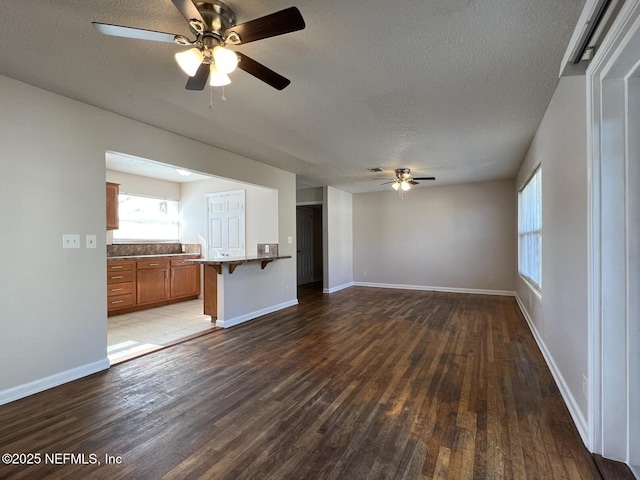 unfurnished living room with ceiling fan, a textured ceiling, and dark hardwood / wood-style flooring