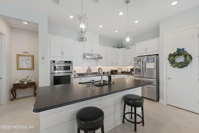 kitchen with an island with sink, appliances with stainless steel finishes, white cabinets, and backsplash