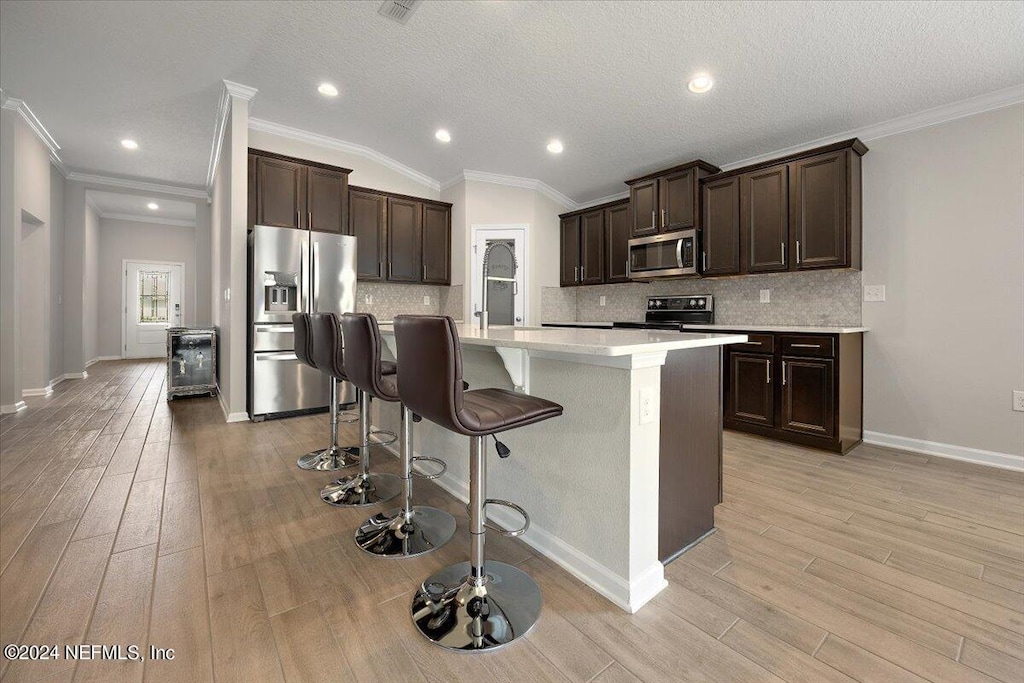 kitchen with crown molding, appliances with stainless steel finishes, a breakfast bar, and a center island with sink