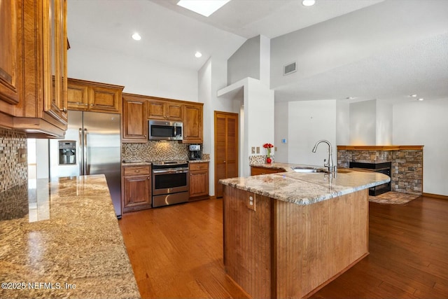 kitchen with appliances with stainless steel finishes, dark hardwood / wood-style floors, a stone fireplace, sink, and light stone counters