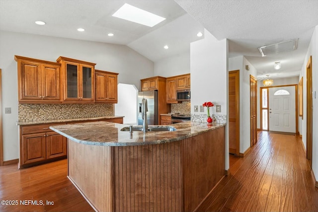 kitchen with sink, stainless steel appliances, vaulted ceiling with skylight, stone countertops, and kitchen peninsula