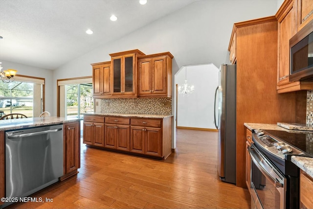 kitchen featuring vaulted ceiling, decorative backsplash, stainless steel appliances, light stone countertops, and an inviting chandelier