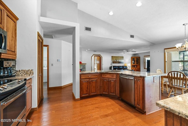 kitchen featuring pendant lighting, stainless steel appliances, light stone countertops, vaulted ceiling, and kitchen peninsula