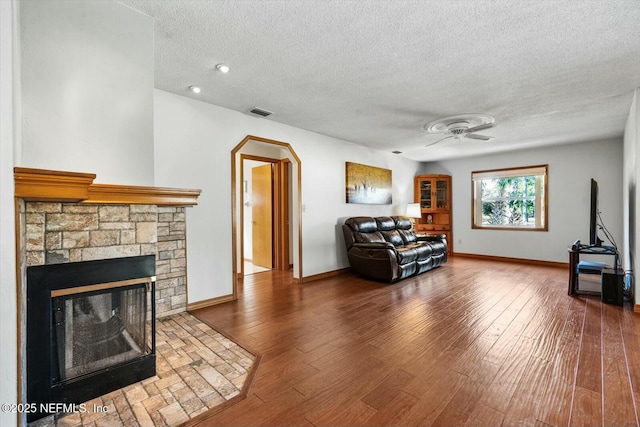 living room featuring a fireplace, a textured ceiling, wood-type flooring, and ceiling fan