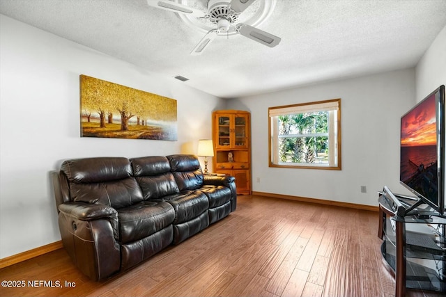 living room featuring hardwood / wood-style flooring, ceiling fan, and a textured ceiling