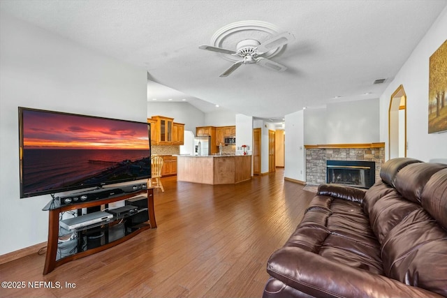 living room featuring lofted ceiling, a brick fireplace, a textured ceiling, dark hardwood / wood-style flooring, and ceiling fan