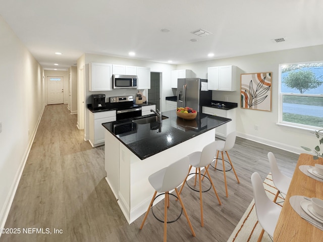 kitchen with stainless steel appliances, white cabinets, and a center island with sink