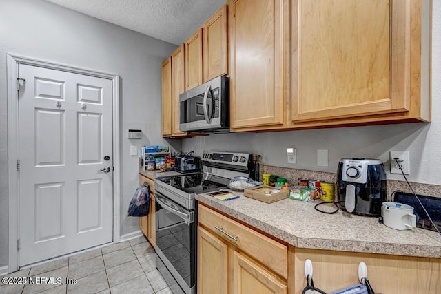 kitchen with light tile patterned floors, light brown cabinets, a textured ceiling, and appliances with stainless steel finishes