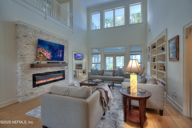 living room featuring a stone fireplace, light wood-type flooring, built in features, and a high ceiling