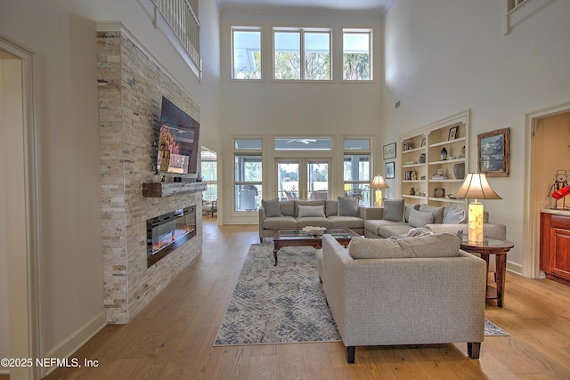 living room with light hardwood / wood-style flooring, a towering ceiling, a fireplace, and built in features