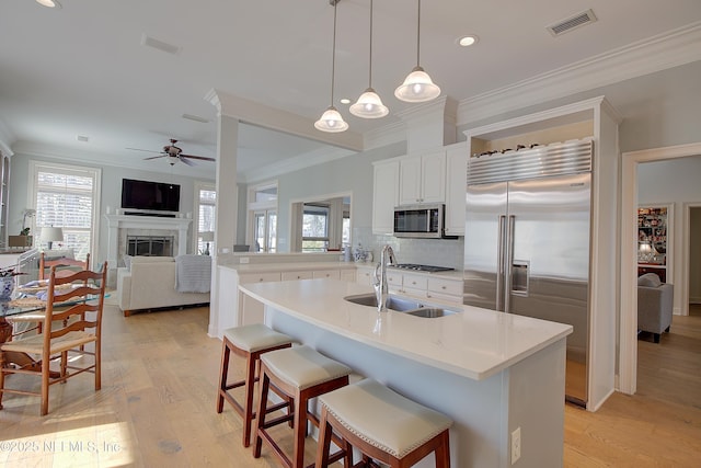 kitchen featuring sink, white cabinetry, decorative light fixtures, stainless steel appliances, and a kitchen island with sink