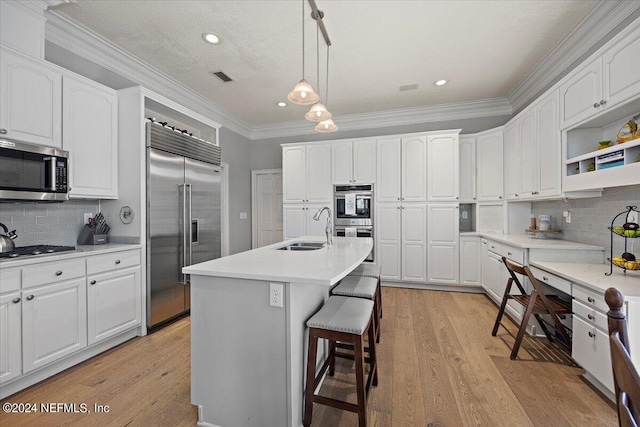 kitchen with white cabinetry, tasteful backsplash, appliances with stainless steel finishes, an island with sink, and pendant lighting