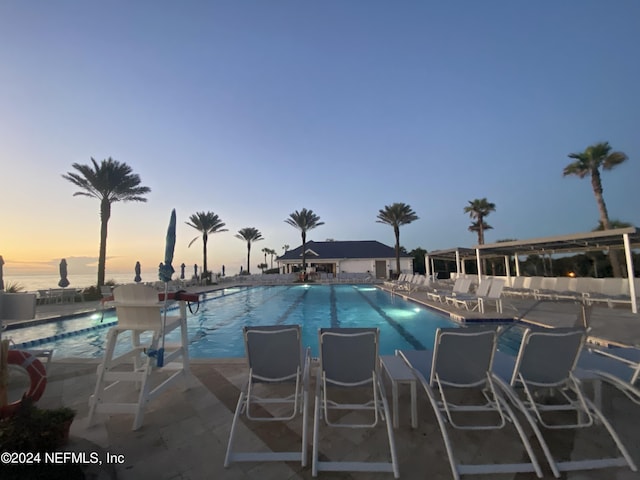 pool at dusk with a water view and a patio area