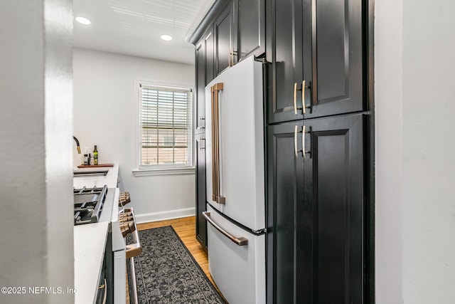 kitchen featuring high quality fridge, stainless steel gas stovetop, sink, light stone counters, and light hardwood / wood-style flooring