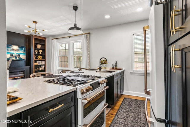 kitchen with sink, light stone counters, hanging light fixtures, fridge, and range with two ovens