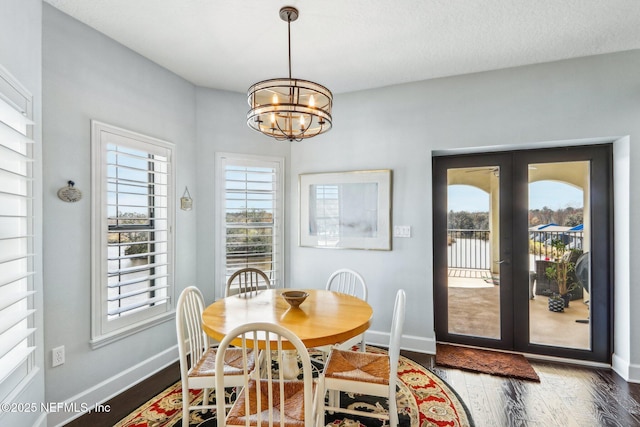 dining space with a wealth of natural light, a notable chandelier, dark hardwood / wood-style flooring, and french doors