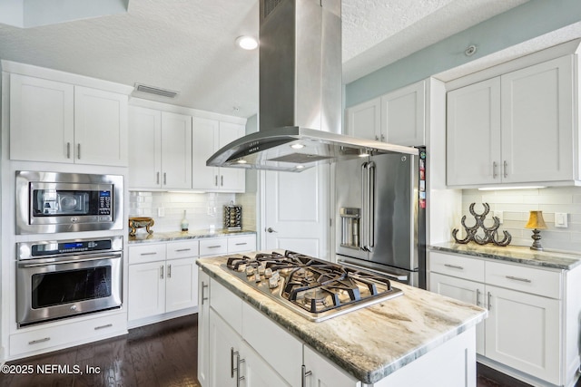 kitchen with island exhaust hood, appliances with stainless steel finishes, white cabinets, and light stone counters