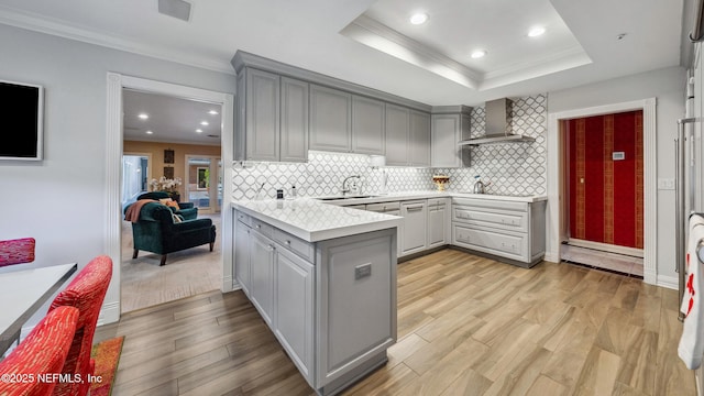 kitchen featuring gray cabinetry, kitchen peninsula, light hardwood / wood-style floors, and wall chimney exhaust hood