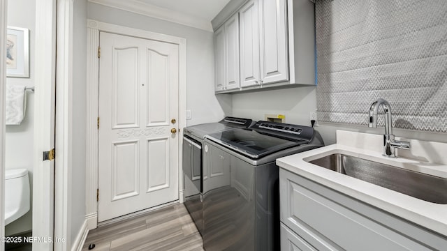 laundry room with washer and dryer, sink, cabinets, light hardwood / wood-style floors, and crown molding