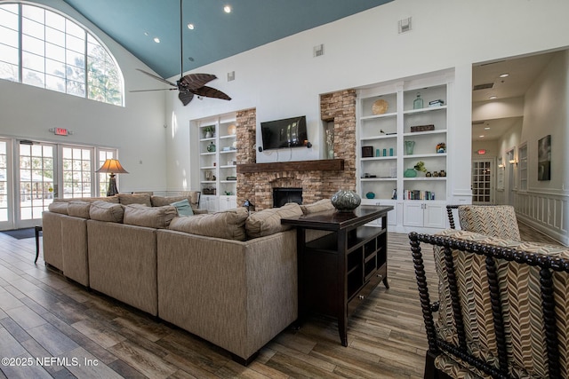 living room with dark hardwood / wood-style flooring, built in features, a towering ceiling, ceiling fan, and a fireplace