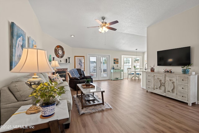 living room featuring hardwood / wood-style flooring, ceiling fan, a textured ceiling, vaulted ceiling, and french doors