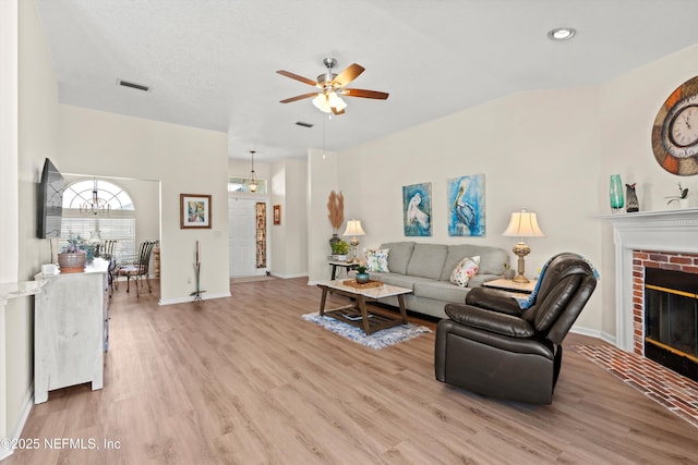 living room with lofted ceiling, ceiling fan, a fireplace, a textured ceiling, and light wood-type flooring