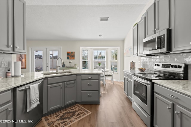 kitchen featuring pendant lighting, sink, gray cabinets, appliances with stainless steel finishes, and light stone countertops