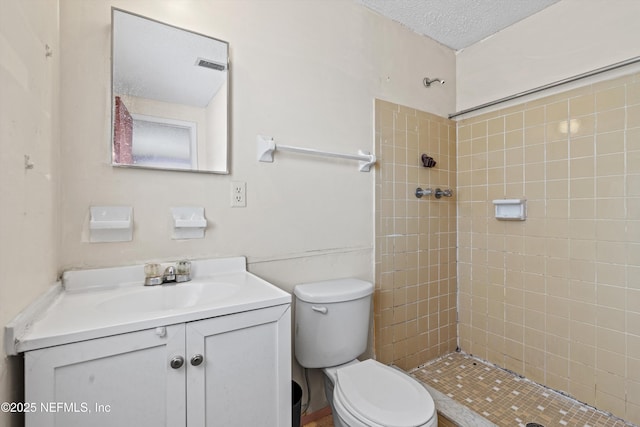 bathroom featuring a tile shower, vanity, a textured ceiling, and toilet