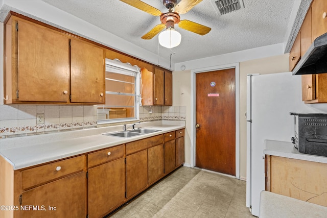 kitchen with sink, ceiling fan, a textured ceiling, decorative backsplash, and white fridge