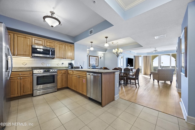 kitchen with light tile patterned flooring, ornamental molding, appliances with stainless steel finishes, kitchen peninsula, and pendant lighting