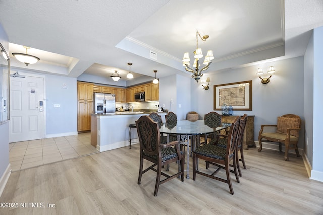 dining room featuring sink, ornamental molding, a notable chandelier, a tray ceiling, and light wood-type flooring