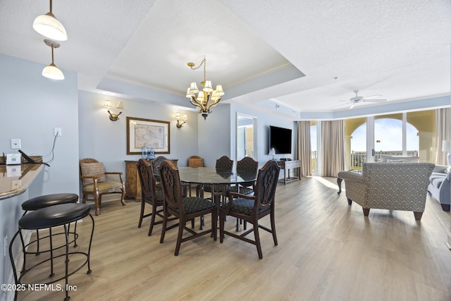 dining area with a tray ceiling, ceiling fan with notable chandelier, a textured ceiling, and light wood-type flooring