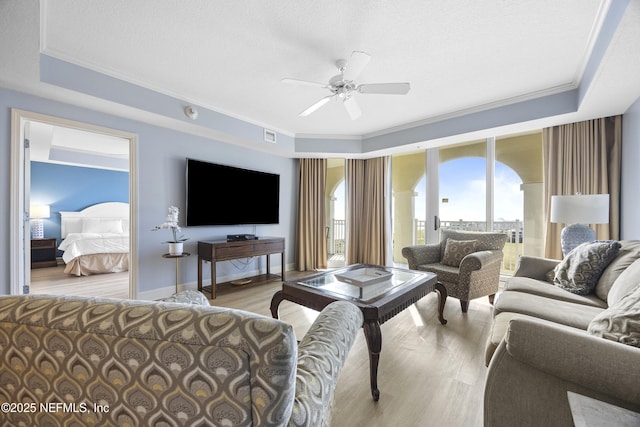 living room featuring crown molding, light hardwood / wood-style flooring, ceiling fan, a textured ceiling, and a raised ceiling